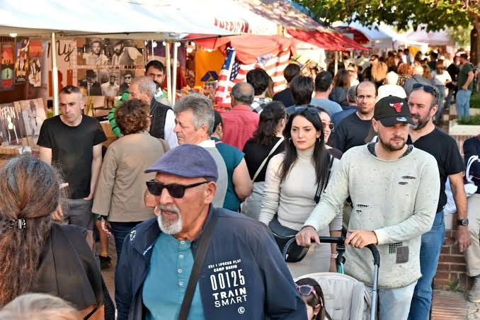 Une rue en fête : la foule circule entre les étals et les auvents d'un marché animé