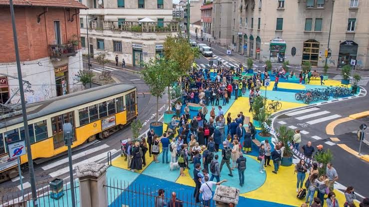 Vue en hauteur d'une place publique aux couleurs vives, pleine de passants
