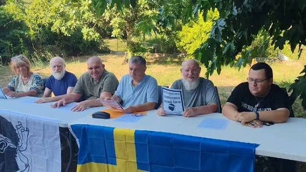 Des anciens assis côte à côte à une longue table dressée en plein air, sous les arbres